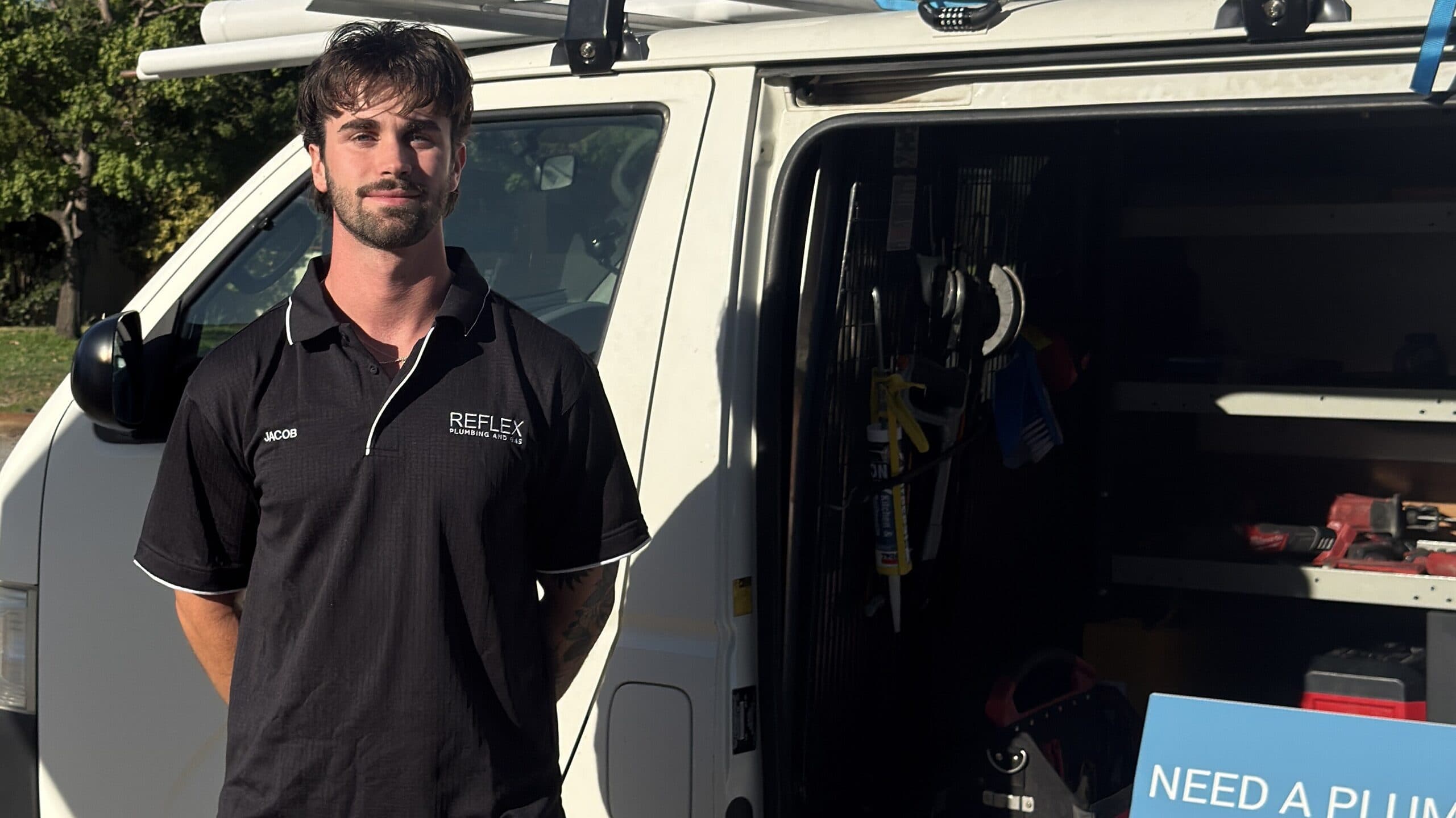 Jacob beside the Reflex Plumbing and Gas van on a residential street in Perth