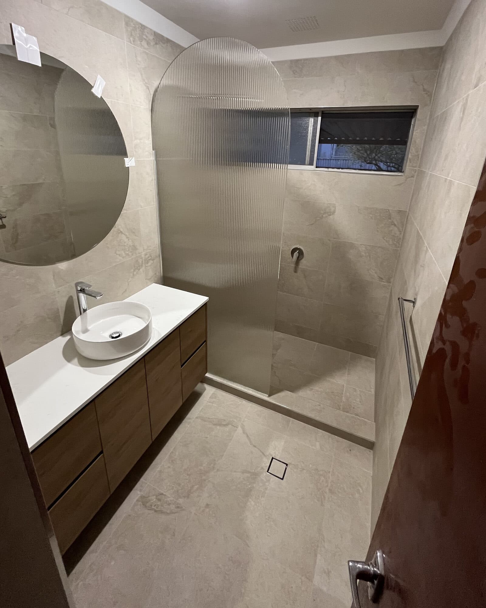 A finished bathroom renovation with a timber vanity, vessel basin and fluted shower screen