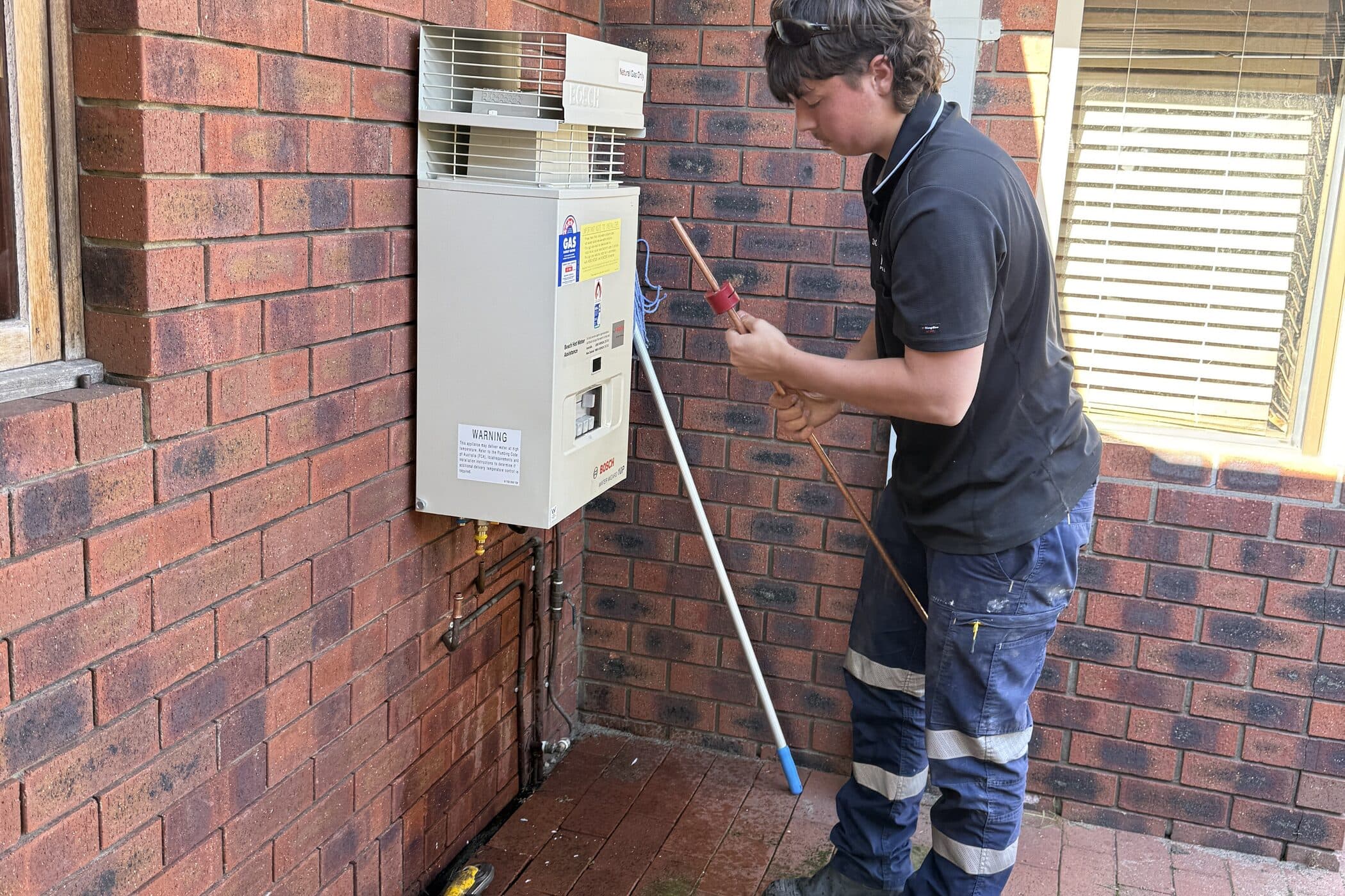 A Reflex plumber working on a gas hot water unit